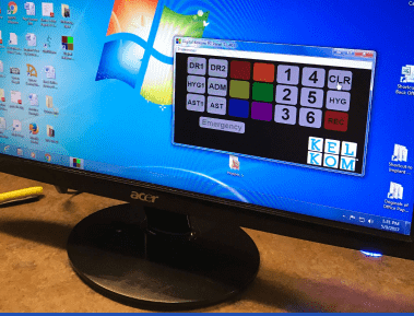 A computer monitor displays a Windows desktop with various icons, alongside a prominent software interface for emergency communications.