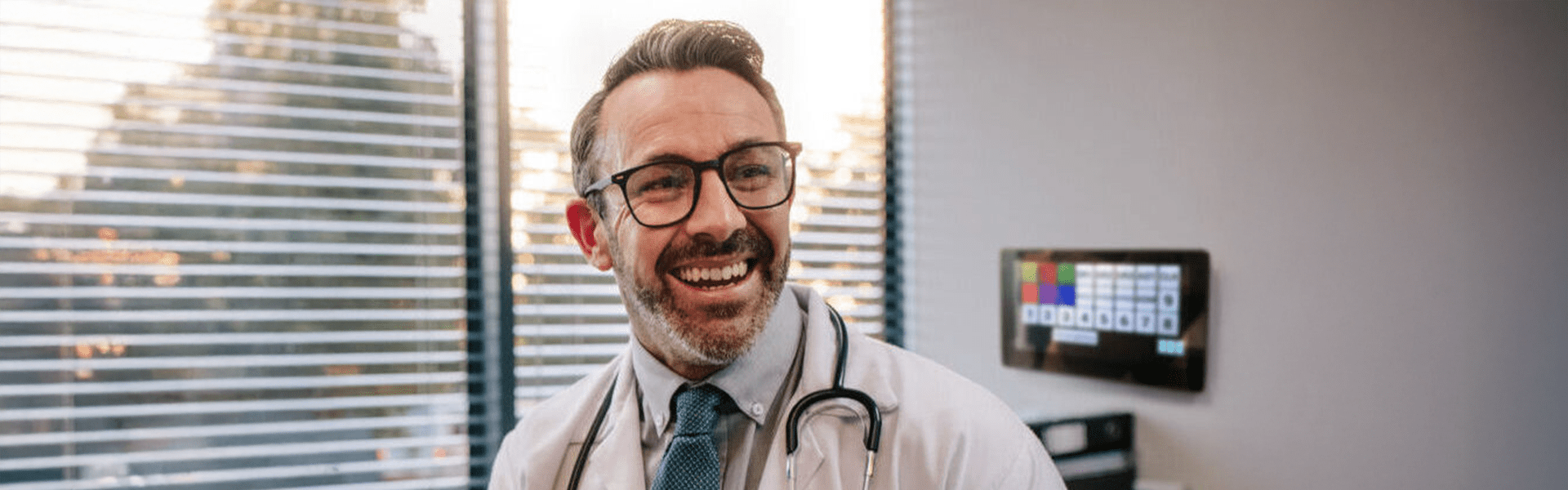 Smiling mature male doctor with digital tablet in his office.